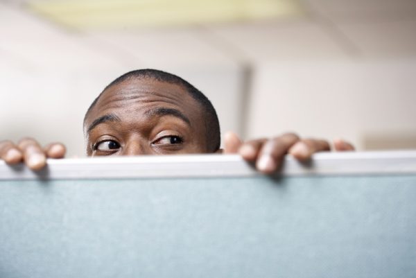 Businessman peeking over cubicle wall