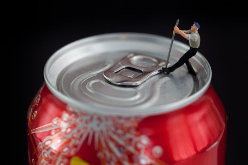 Tiny worker uses a crowbar to open a jar of Coca-Cola